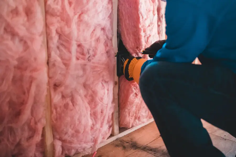 Vakman brengt roze steenwol-isolatie aan in een dakconstructie