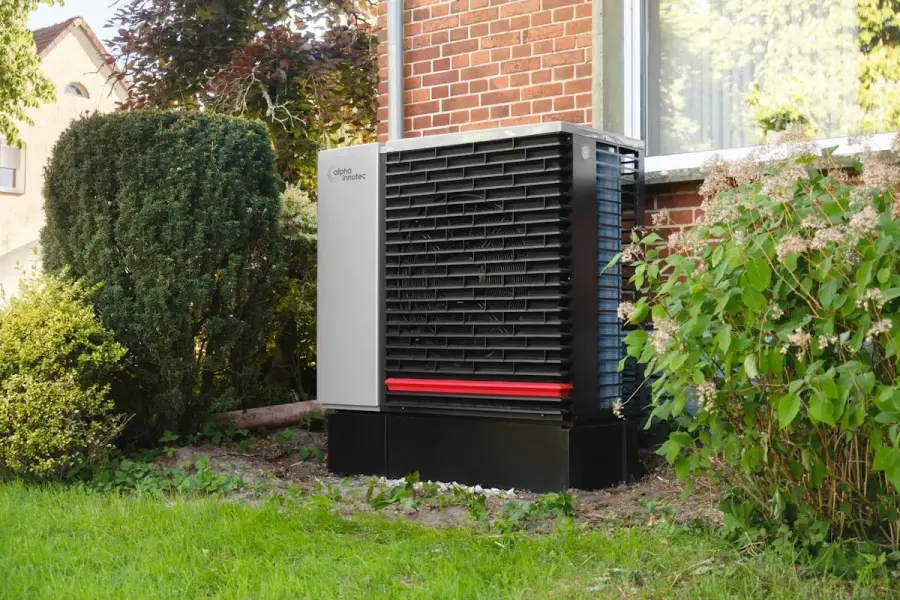 Buitenunit van een warmtepomp naast een bakstenen woning